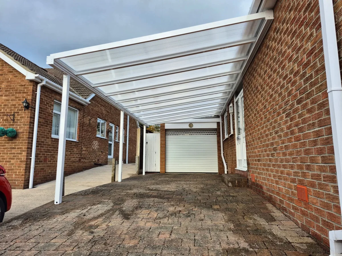 White-framed carport with polycarbonate roofing in front of a garage