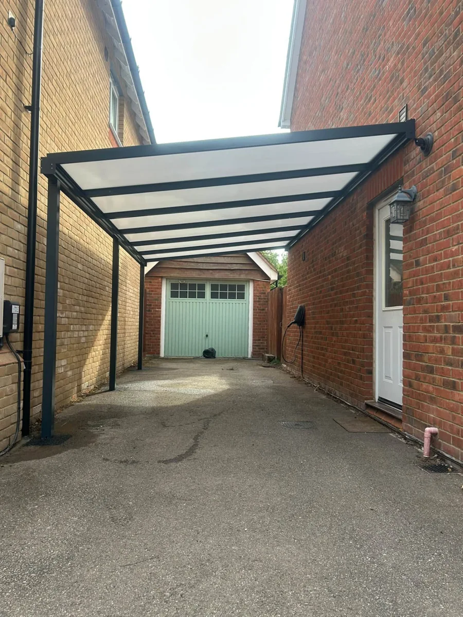 Dark-framed polycarbonate carport extending towards a garage