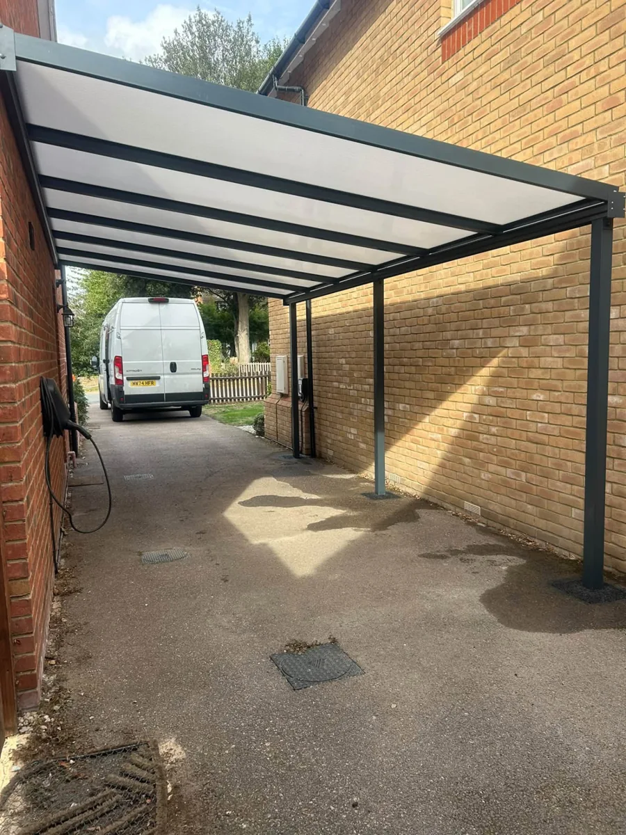 Dark-framed carport covering a driveway between two brick properties