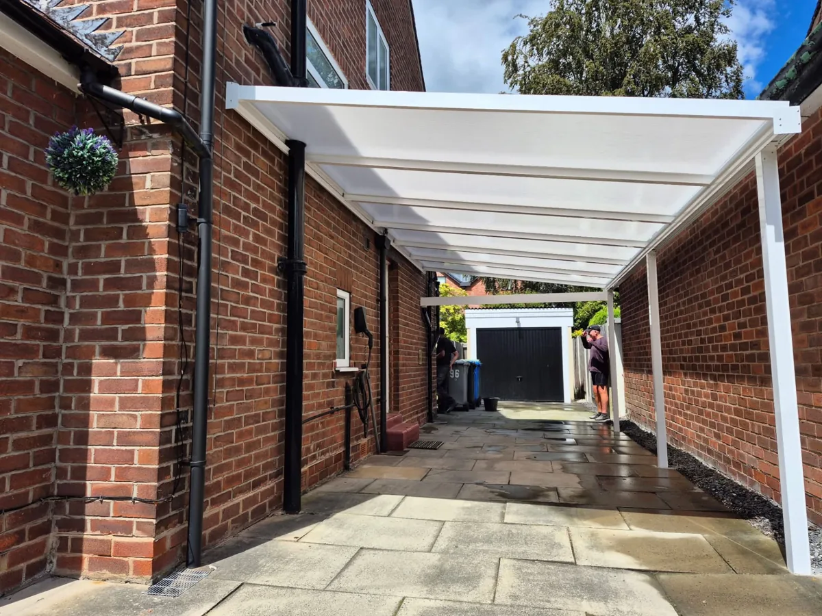 White canopy frame and light-transmitting roof over a paved driveway